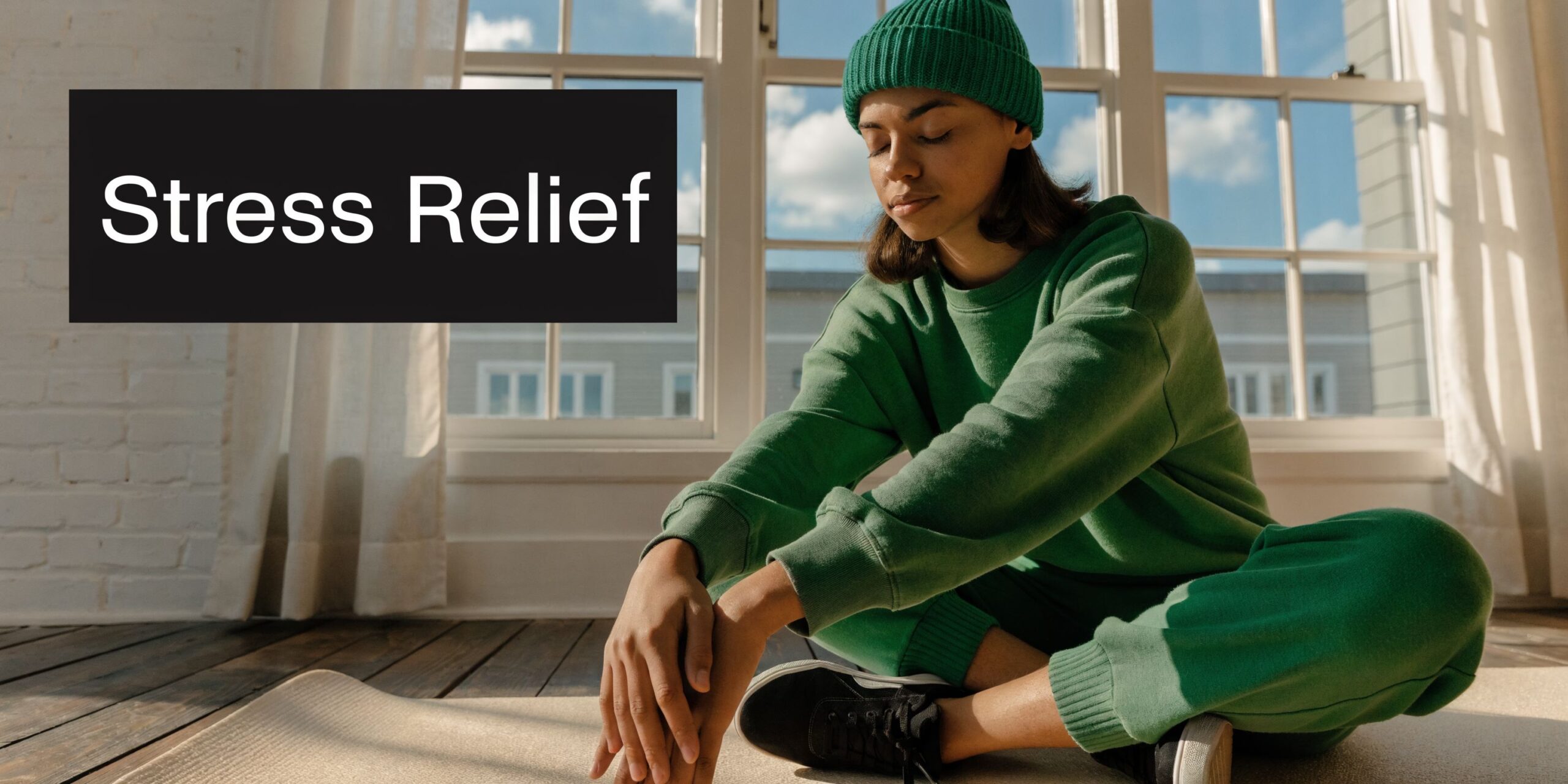 A person wearing a green beanie and matching sweatshirt practices mindful meditation while sitting on a mat.