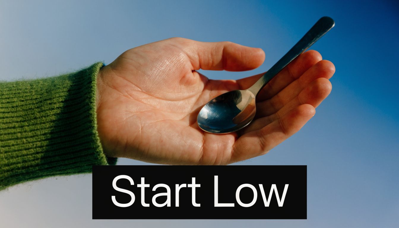 A human hand holding a small metal spoon against a bright blue sky background.